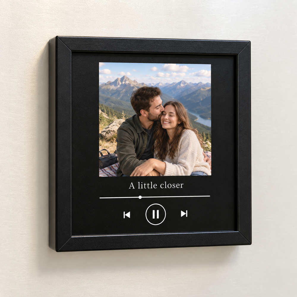 Black framed music fridge magnet with a mountain picnic couple portrait and A little closer caption.